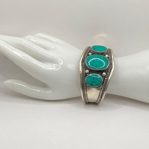 May include: Silver bracelet with turquoise stones. The bracelet is open and has a hinged closure.