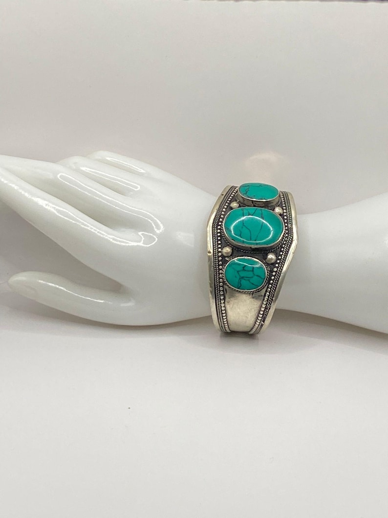 May include: Silver bracelet with turquoise stones. The bracelet is open and has a hinged closure.