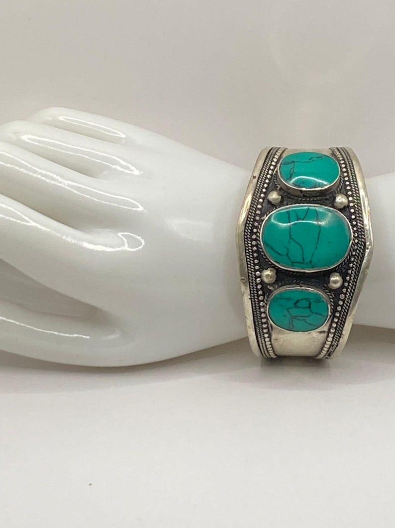 May include: Silver bracelet with three turquoise stones set in a decorative design.