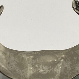 May include: Silver bracelet with a textured, curved design. The bracelet is open on one side and has a smooth, polished finish.