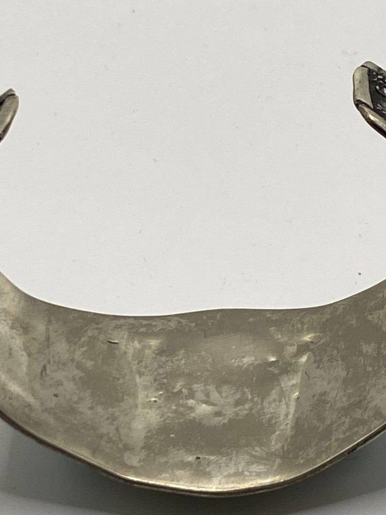 May include: Silver bracelet with a textured, curved design. The bracelet is open on one side and has a smooth, polished finish.