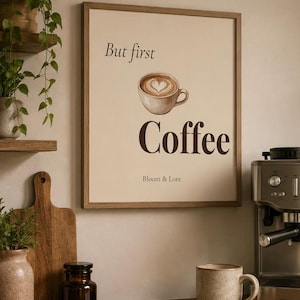 Könnte beinhalten: Ein rechteckiges Wandbild in einem hellen Holzrahmen mit beigem Hintergrund, einer Aquarellillustration einer Kaffeetasse mit Herz-Latte-Art und dem Text "But first Coffee" in Dunkelbraun, mit "Bloom & Lore" darunter gedruckt.