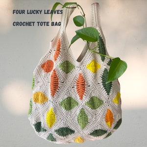 May include: A crocheted tote bag with a white background and colorful leaf designs in shades of green, orange, and yellow. The bag has a simple design and is made with a thick yarn. The text "FOUR LUCKY LEAVES CROCHET TOTE BAG" is printed on the top of the image.