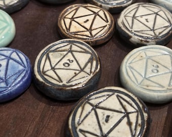 May include: A collection of ceramic game pieces, each with a geometric design and a number. The pieces are primarily cream-colored with dark brown and blue accents. The pieces are arranged on a dark wooden surface.