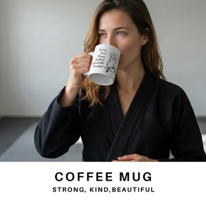 May include: White coffee mug with black text and a line drawing of a woman. The mug has the words "Loving, Real, Strong, Beautiful, Unbreakable, Beautiful" printed on it. The words "COFFEE MUG" and "STRONG, KIND, BEAUTIFUL" are also displayed.