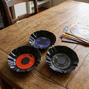 Könnte beinhalten: Drei Schalen aus wiederverwerteten Schallplatten mit gewelltem Rand. Eine Schale hat ein rotes Polydor-Label, eine ein violettes Decca-Label und eine ein schwarzes RCA Victor-Label. Jede Schale besitzt eine dunkle, kreisförmige Mitte.