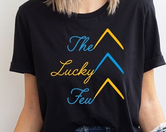 May include: A black t-shirt with the text "The Lucky Few" in yellow and blue lettering. The text is stylized with arrows pointing upwards.