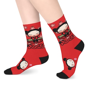 May include: Red socks featuring a cartoon character design. The socks have black heels and toes, and the character is depicted with a smiling face and a floral accent. The word "Pucca" is also visible on the socks.
