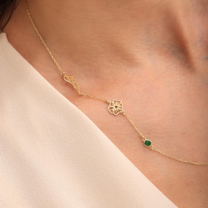 May include: A gold necklace with a wing charm, a flower pendant, and a small green gemstone. The necklace is shown on a person's neck, highlighting its elegant design and intricate details. The necklace is a beautiful piece of jewellery.