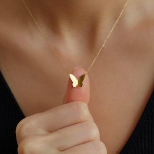 Op de afbeelding: Een delicate goudkleurige vlinderhangerketting. De vlinderbedel is klein en rust op een dunne ketting. De ketting wordt gepresenteerd tegen een neutrale achtergrond.