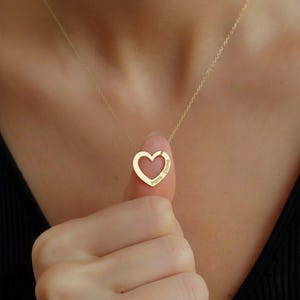 Op de afbeelding: Een goudkleurige ketting met een fijne schakelketting en een hartvormige hanger. De hanger is een open hartje met de namen Pierre en Emina gegraveerd langs de rechterkant van de hartrand in een strak, schreefloos lettertype.