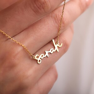 Op de afbeelding: Een delicate goudkleurige ketting met de naam "Sarah" in cursief schrift. De hanger hangt aan een fijne ketting, waardoor een gepersonaliseerd en elegant accessoire ontstaat. De ketting wordt getoond tegen een zachte achtergrond.