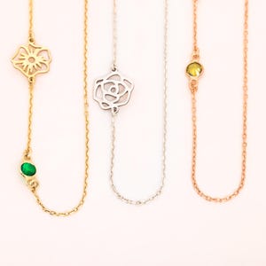 May include: Three necklaces with different pendant designs. The first is gold with a flower and green gemstone. The second is silver with a rose. The third is rose gold with a yellow gemstone. All have fine chain links.