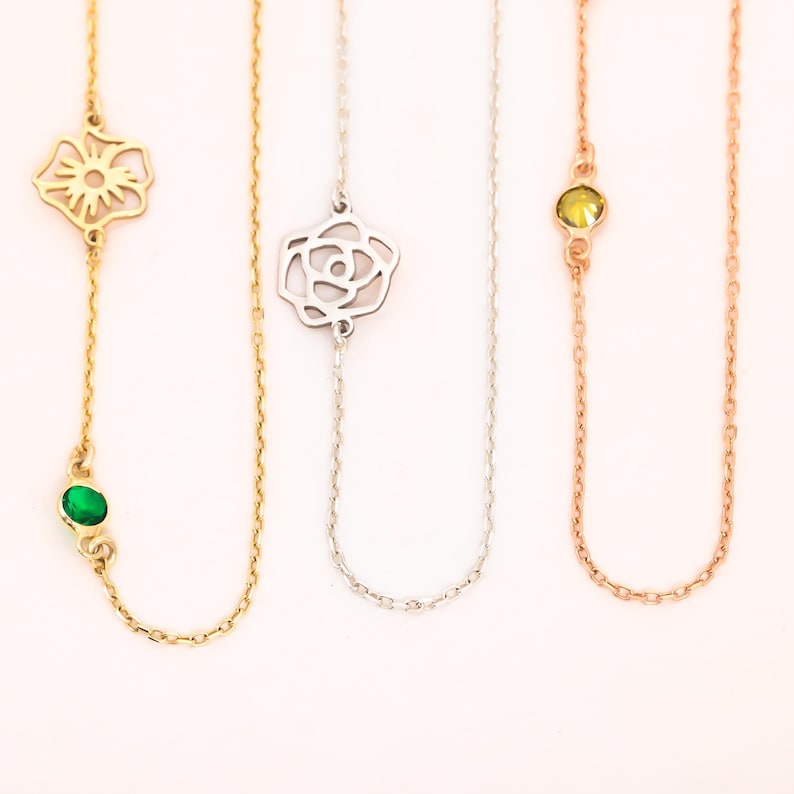 May include: Three necklaces with different pendant designs. The first is gold with a flower and green gemstone. The second is silver with a rose. The third is rose gold with a yellow gemstone. All have fine chain links.