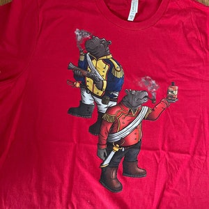 May include: Red t-shirt with a graphic of two hippos dressed in military uniforms. One hippo is holding a gun and the other is holding a bottle of liquor and a pipe.