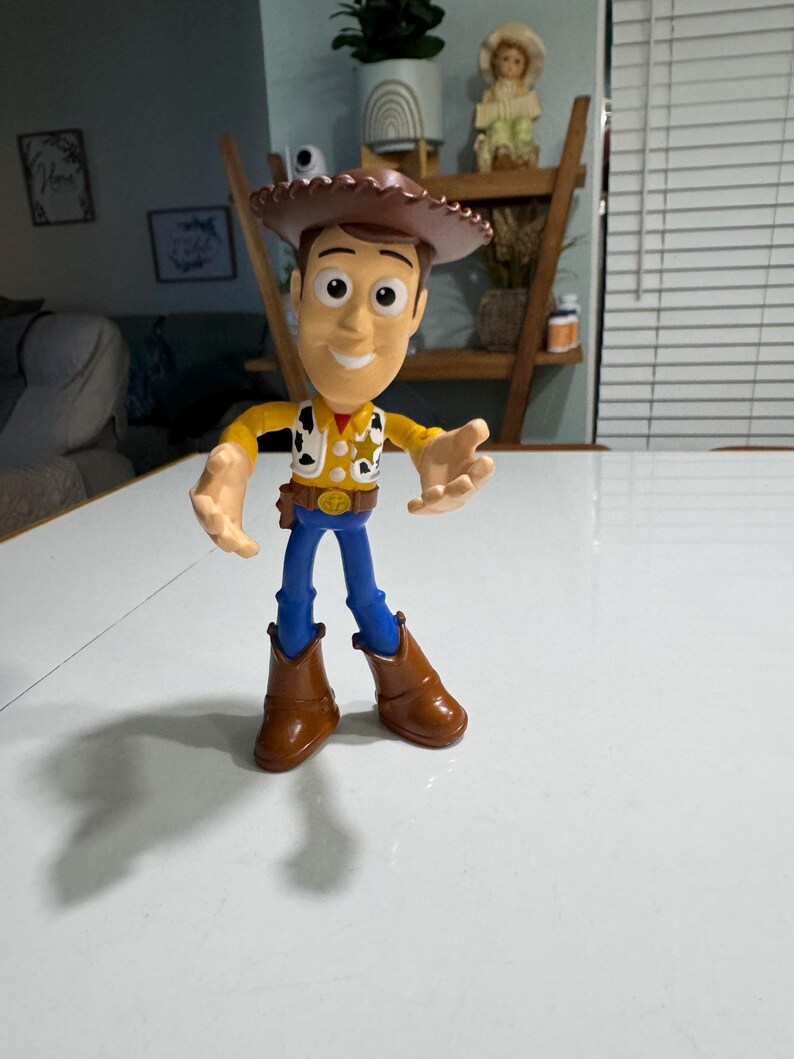 May include: A plastic toy figure of Woody from the Toy Story franchise. Woody is wearing his signature brown cowboy hat, yellow vest, blue jeans, and brown boots. He has a friendly expression on his face.