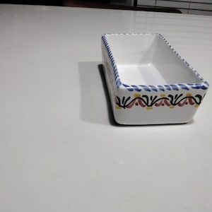 May include: A white ceramic rectangular dish with a blue, yellow, and pink floral design around the rim.