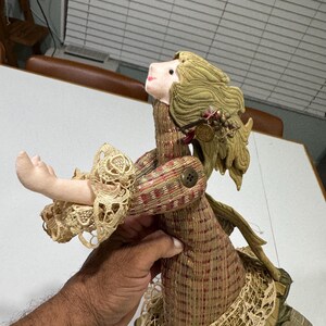 May include: A handmade doll with a plaid dress, lace trim, and a green fabric head with blonde hair. The doll is holding out its arm and has a button on its chest.