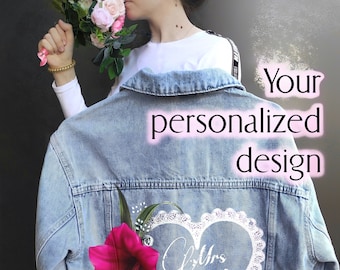 Pode incluir: Uma jaqueta de ganga azul claro com um design de coração branco com o texto "Mrs. Bride". Uma flor rosa está no lado esquerdo do coração.