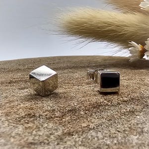 May include: A pair of silver cube stud earrings. The earrings are small and have a simple, modern design.