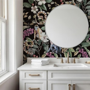May include: A bathroom vanity with a white countertop, sink, and drawers. A round mirror hangs on a wall with a dark floral and animal print. The print features monkeys, snakes, flowers, and berries. A stack of white towels sits on the counter.