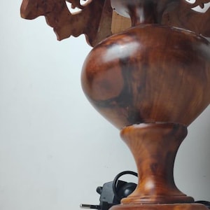 May include: A wooden table lamp with a carved shade featuring intricate floral cutouts. The lamp has a bulbous base and a dark brown finish, with a power cord and plug visible.
