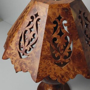May include: A wooden lampshade with a unique, patterned design. The shade is a warm brown color with intricate cut-out patterns. The base is a matching brown, and the overall design is decorative.