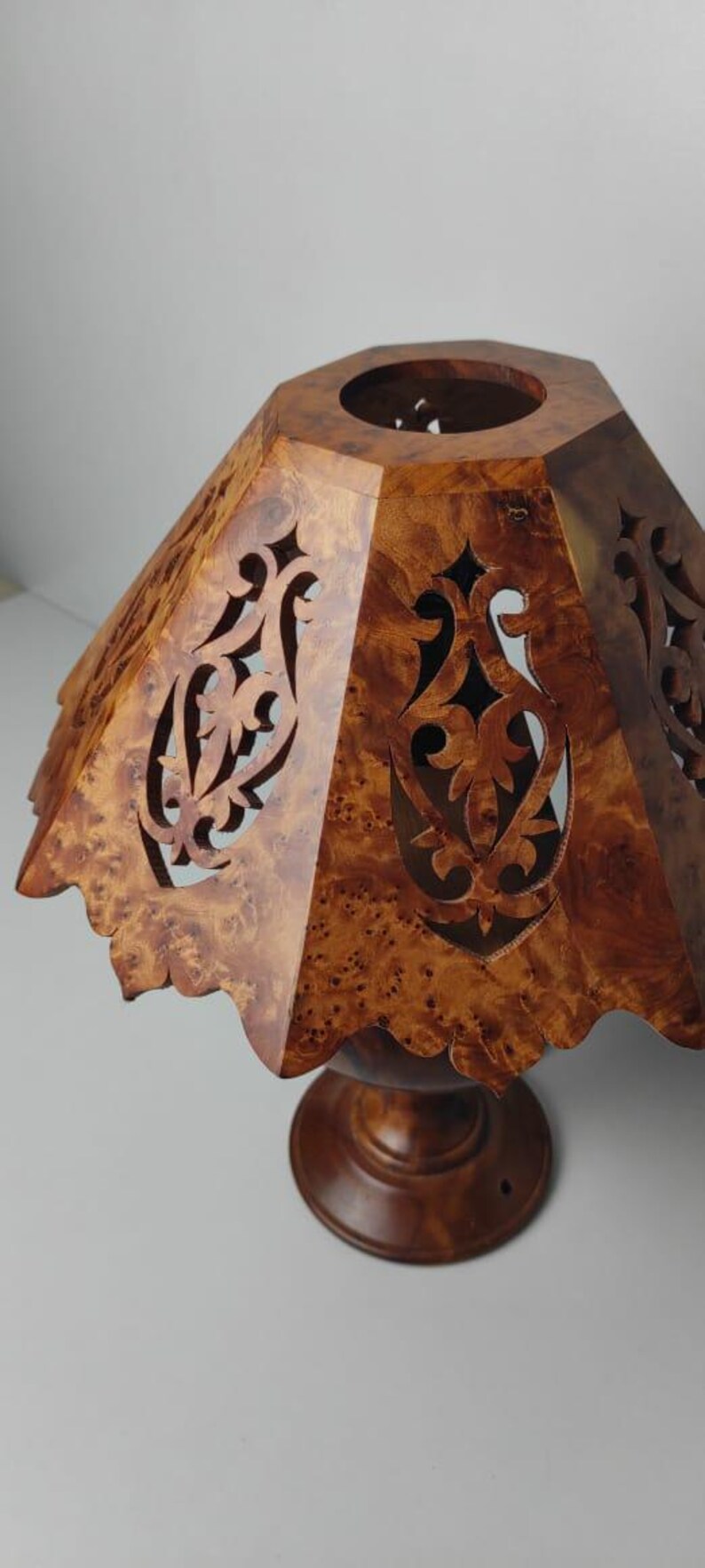 May include: A wooden lampshade with a unique, patterned design. The shade is a warm brown color with intricate cut-out patterns. The base is a matching brown, and the overall design is decorative.