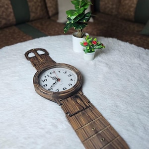 May include: A wooden wristwatch-shaped clock with a white clock face and black numerals. The clock's hands are black with a red second hand. The watch band is made of wood and has a rustic appearance.