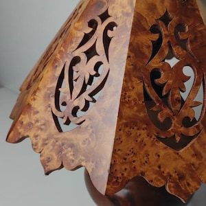 May include: A wooden lamp with a decorative shade. The shade is made of a light brown wood with intricate cut-out designs. The lamp base is a darker brown, and the overall design is elegant and handcrafted.