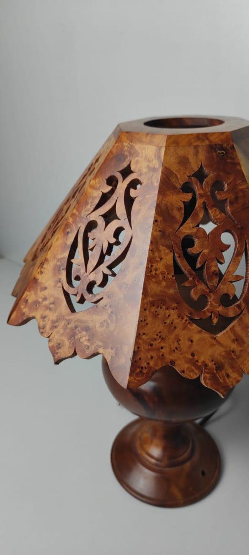 May include: A wooden lamp with a decorative shade. The shade is made of a light brown wood with intricate cut-out designs. The lamp base is a darker brown, and the overall design is elegant and handcrafted.