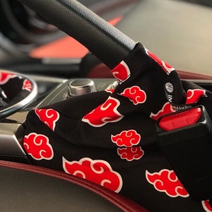 May include: Black and red car gear shift boot cover with a repeating pattern of red clouds on a black background. The cover has a black strap with a red buckle. The text "and love focus" is visible on the strap.