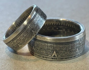 May include: Two silver rings made from coins with intricate designs. The rings are stacked on top of each other.