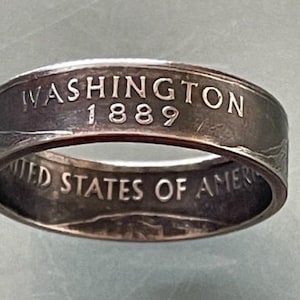 May include: Silver ring made from a 1889 Washington quarter. The ring features the words "United States of America" and "Washington 1889" engraved on the band.