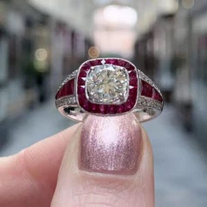 Peut inclure: Une bague en argent avec un grand diamant rond et clair entouré d'un halo de rubis rouges. La bande de la bague est également sertie de diamants et de rubis plus petits.