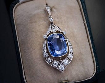 May include: A vintage pendant featuring a large, cushion-cut sapphire surrounded by a halo of smaller diamonds. The pendant is crafted in platinum and has a delicate, ornate design.