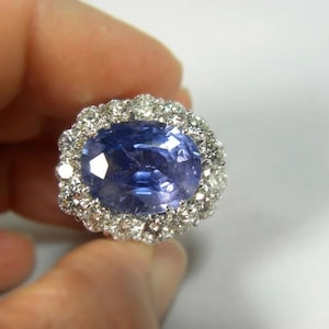May include: A large oval sapphire ring with a halo of smaller diamonds set in white metal.