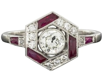 Könnte beinhalten: Ein Platinring mit hexagonalem Design, der einen runden Diamanten in der Mitte zeigt, umgeben von Baguette-geschliffenen Rubinen und kleineren Diamanten.
