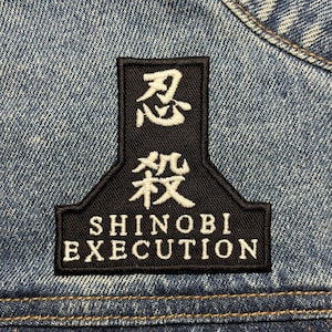 Pode incluir: Patch bordado preto e branco com caracteres japoneses e o texto "Shinobi Execution" em uma jaqueta jeans.