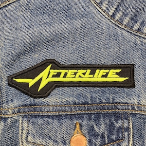 May include: A black and yellow embroidered patch with the word "AFTERLIFE" in a stylized font. The patch is sewn onto a blue denim jacket.