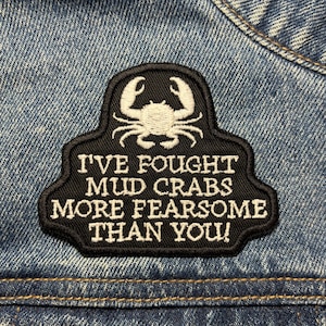 Op de afbeelding: Zwart-witte geborduurde patch met een krabdesign en de tekst "Ik heb modderkrabben bevochten die angstaanjagender zijn dan jij!"