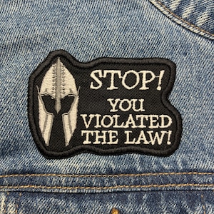 May include: Black and white embroidered patch with a helmet and the text "STOP! YOU VIOLATED THE LAW!"