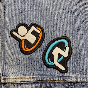 Könnte beinhalten: Zwei gestickte Aufnäher auf einer blauen Jeansjacke. Die Aufnäher sind schwarz mit weißen Umrissen und zeigen eine stilisierte Figur, die im Kreis läuft. Ein Aufnäher hat einen orangen Kreis, der andere einen blauen Kreis.