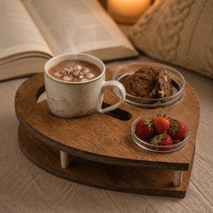 Könnte beinhalten: Ein herzförmiges Serviertablett aus Holz mit dunkelbrauner Oberfläche und vier kurzen zylindrischen Beinen. Das Tablett hat Aussparungen für eine Keramiktasse mit heißer Schokolade, eine Glasschale mit Schokoladenkeksen und frische Erdbeeren.