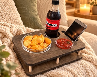 May include: A dark brown wooden snack tray with two levels, featuring circular cutouts for a bottle of Bianca soda and a smartphone. The tray holds a clear glass bowl filled with potato chips and a smaller glass bowl containing red salsa.