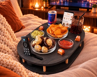 May include: A dark wood oval couch tray with short legs featuring integrated slots for a remote control, a beverage can, and a smartphone. The tray holds a bowl of tortilla chips, a bowl of guacamole, a bowl of salsa, and gold-wrapped chocolates.