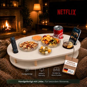 Puede incluir: Una bandeja de sofá ovalada de madera blanca con ranuras integradas para un mando, una lata de bebida y un smartphone. La superficie contiene cuatro cuencos de cristal con frutos secos, aceitunas, queso y patatas. Una etiqueta dice PREMIUM COUCH BAR.
