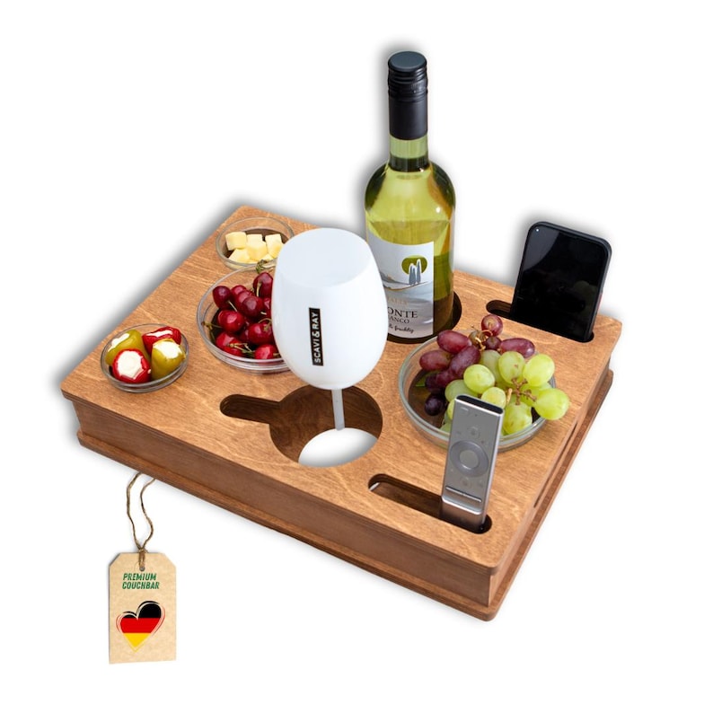 May include: A wooden couch tray with cutouts for a wine glass, bottle, and phone. It holds small bowls of snacks, a bottle of white wine, and a remote. The tray has a tag that says "Premium Couchbar".