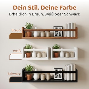 May include: Three wall-mounted floating shelves in brown, white, and black finishes. Each shelf features a horizontal front rail, holding potted green plants, white vases, small jars, framed photos, and books. Text reads: Dein Stil. Deine Farbe.