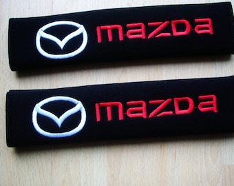 A pair of beautifully embroidered Mazda soft seat belt covers